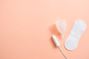 Obraz premium Menstrual hygiene products including tampon, menstrual cup and sanitary pad on peach background