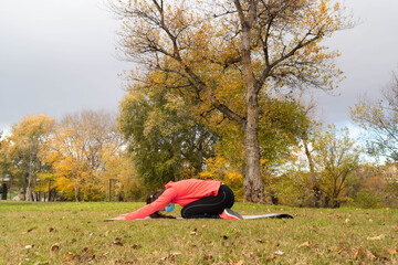 Sporty dressed woman does back stretches on a mat in the park wearing a mask to protect herself from the coronavirus