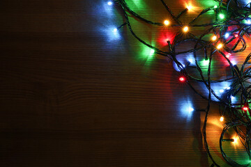 Colorful Christmas lights on wooden table, top view. Space for text