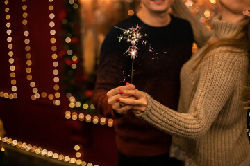 young man and woman hug and hold sparklers on the background of Christmas lights