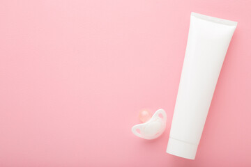 White cream tube and baby soother on light pink table background. Pastel color. Care about clean and soft body skin. Daily children beauty product. Closeup. Empty place for text. Top down view.