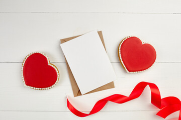Greeting card mockup with paper envelope and red ribbon and heart shaped ginger snap cookie on white table