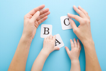 Young adult mother hands showing white cards of letters to baby on light blue table background....