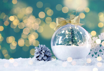 Beautiful transparent Christmas ornament with small fir tree on snow against blurred lights, bokeh effect. Space for text