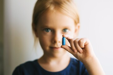 Close up portrait of a pretty little girl taking pills. Child with pills. - 398767349