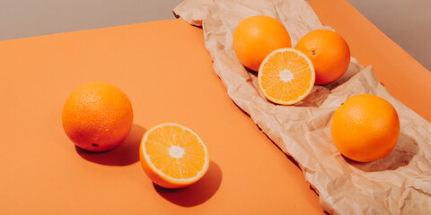 Oranges scattered on a ginger table against a background of crumpled kraft paper. Conceptual minimalistic summer still life with juicy citrus fruits. Hard Light.