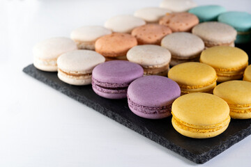Macarons are laid out on a black slate in beautifully colored rows.