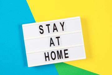 Lightbox with text STAY AT HOME on yellow, green and light blue background. Top view