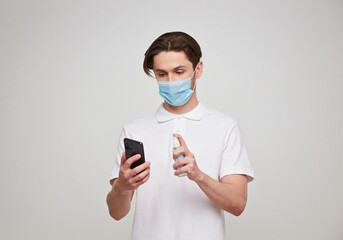 Fototapeta na wymiar European man in a mask disinfects the phone. Conceptual photo on the theme of the covid-2019 pandemic.