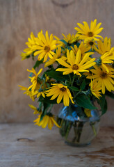 A bouquet of yellow Jerusalem artichoke flowers in a glass vase on a wooden background. Postcard with place for text. A simple wild flower that looks like a chamomile. Copy space.