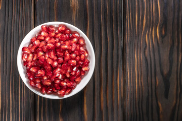 Garnet seeds in white plate on dark wooden background