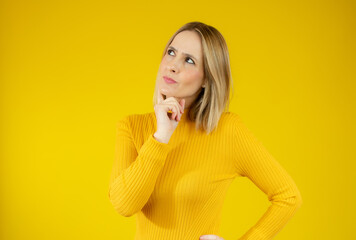 Young woman wearing casual sweater with doubtful gesture over yellow background.