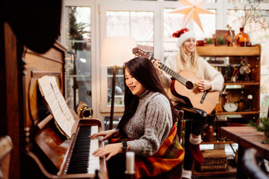 two young women play the piano and guitar in a country house.