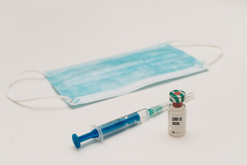 covid-19 vaccine and face mask on white background