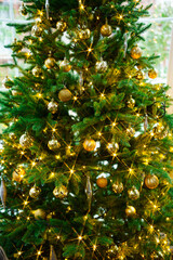 artificial Christmas tree decorated with gold toys and garland bulbs. 