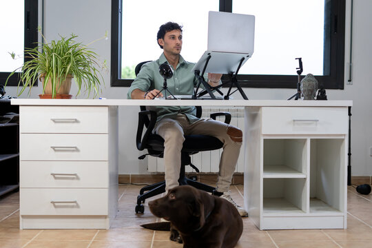 A Young Man Is Working From Home With His Computer In The Office And His Dog Distracts Him