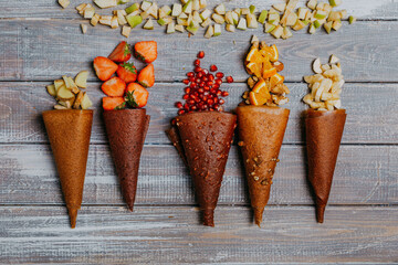 Fruit leather cones with fresh fruits in pieces on the wooden table. No sugar fruit leather cones. Healthy food. Apples, bananas, strawberries, oranges, nuts, black currant, pomegranate top view.