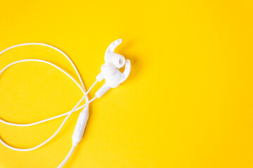 White headphones with a wire on a yellow background. Concept of gadgets.
