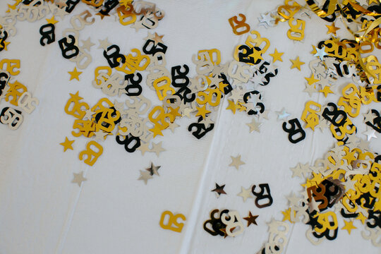 Fiftieth Anniversary Party Black And Gold Confetti Flay Lay On Table With White Tablecloth