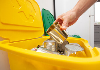The man throws the tin can to the one of three container for sorting garbage