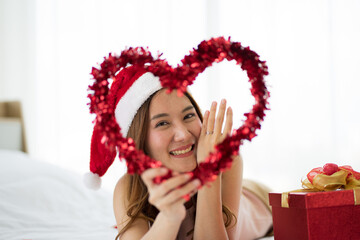 Asian Attractive  young Wolman on bed wearing red Santa hat and red gift box during Christmas holiday. new normal concept. 