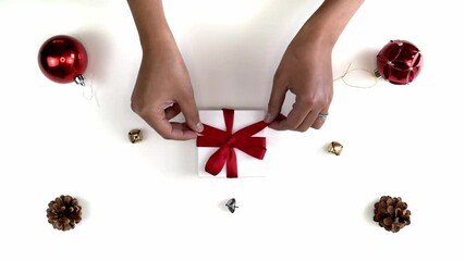 Hand and arm shot of a mixed race African American woman untying a bow on a small white gift box Christmas present wrapped with a red ribbon and bow sitting in middle of festive background.