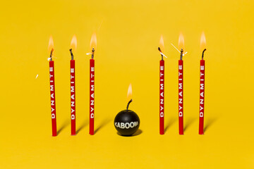 Red dynamite birthday candles burning on a bright yellow background.