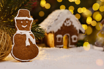 Gingerbread snowman and snow decoration for Christmas and New Year, dark background, selective focus, bokeh. Christmas food. Snowman biscuit. Gingerbread house.