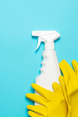 Yellow latex gloves lies on a cleaning spray on blue background, top view, copy space. Cleaning supplies.