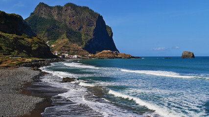 Obraz premium Beautiful view over rocky beach Praia da Maiata on the wild Atlantic coast near village Porto da Cruz in the north of Madeira island, Portugal with the majestic peak of Penha D'Aguia mountain.