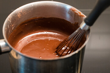 Preparing delicious hot chocolate with a whisk in a metal saucepan. Close up shot of traditional recipe.