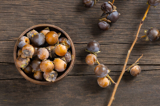 Ripe small persimmon fruit, black date or palm berries with branch on wooden background, (Diospyros lotus), copy space for text