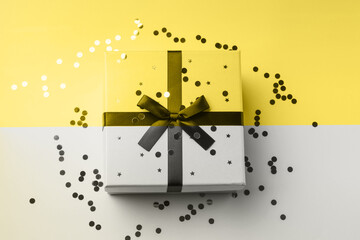 Gift box on gray and illuminating yellow backdrop with sparkling confetti. Christmas, birthday concept