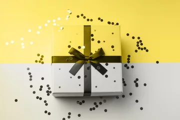 Fotobehang Gift box on gray and illuminating yellow backdrop with sparkling confetti. Christmas, birthday concept © tenkende