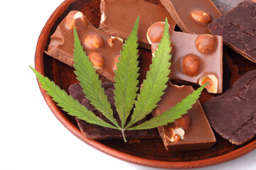 Pieces of chocolate on a saucer with a white isolated background with a green hemp or marijuana leaf. Flat lay. Rectangular CBD Cannabis Chocolate Cookies