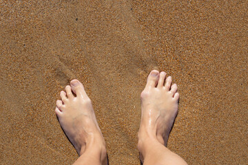 woman's bare feet on the yellow sand. Summer rest. A large bone on the toe of the right foot