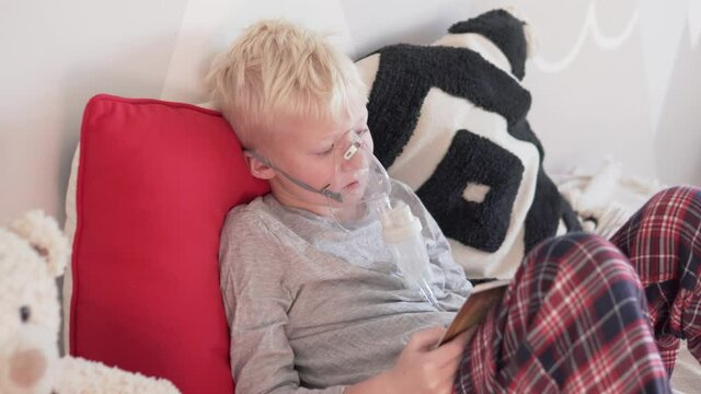 The child makes Inhalation Masked with steam and reads a book at home on the sofa during the disease of covid-19