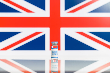 A vial of a covid, coronavirus vaccine with a UK flag on the background. One glass bottle of medicine against British flag