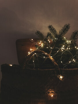 Merry Christmas! Rustic basket with Christmas tree branches in lights on wooden chair in the dark