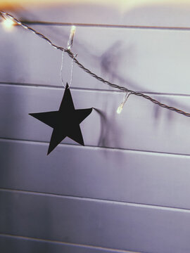Christmas paper star hanging on white wall with garland lights. Aesthetic christmas decor.
