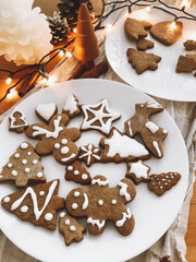 Christmas gingerbread cookies on white plate on rustic wooden table with lights