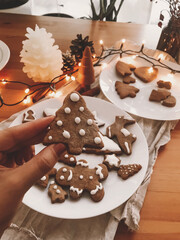Hand holding Christmas tree gingerbread cookie at rustic wooden table with lights