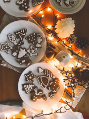 Christmas gingerbread cookies on white plate on rustic wooden table with lights in evening