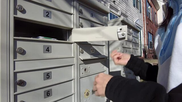 A woman is opening her mailbox inside a cluster of mailboxes for her condo and takes out enveloppes delivered by the postal service. These metal boxes are commonly used for apartments and townhomes.