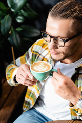 high angle view of man in eyeglasses holding cup of coffee with latte art