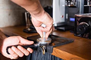 cropped of barista pressing ground coffee in portafilter