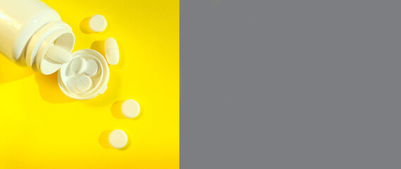 Scattered pills over gray and yellow backdrop. White bottle and white  pills on yellow background.  Health and medicine concept.