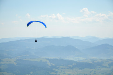 Paraglider flying over the mountains against the blue sky in clear weather. Extreme sport, lifestyle and freedom concept