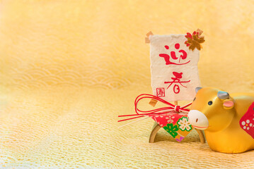 Japanese New Year's Card with handwriting ideograms Geishun or Welcoming Spring on a traditional decoration and a cute Zodiacal animal figurine of cow for the 2021 Year of the Ox on a felt background.