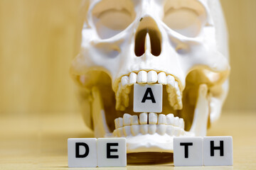 A row of small white plastic tiles, containing the letters forming the word death, placed on a table together with a skull, to represents the concept of death.